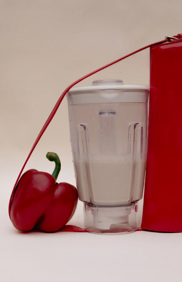 Still life rosso: un peperone e un frullatore trasparente legati da un cordino rosso a un oggetto rosso