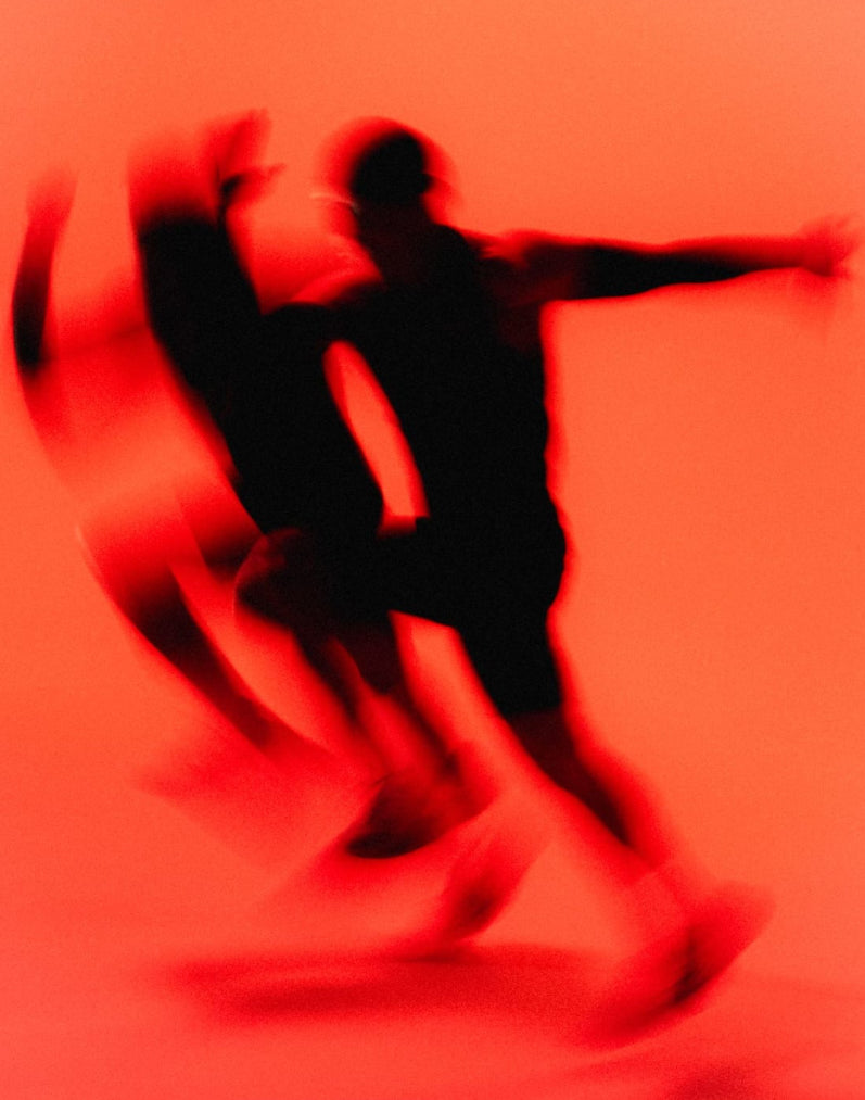 Due figure in movimento, sfocate e in controluce, su fondo rosso arancio